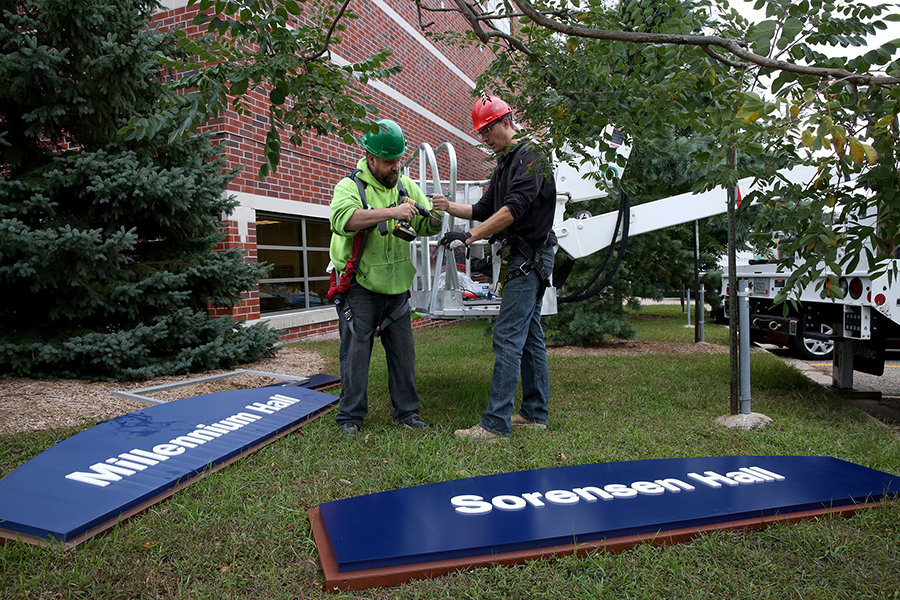 Workers prepare to put up a Sorensen Hall sign after taking down the Millennium Hall sign.