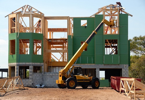 photo of a green home being constructed with a yellow crane located in front