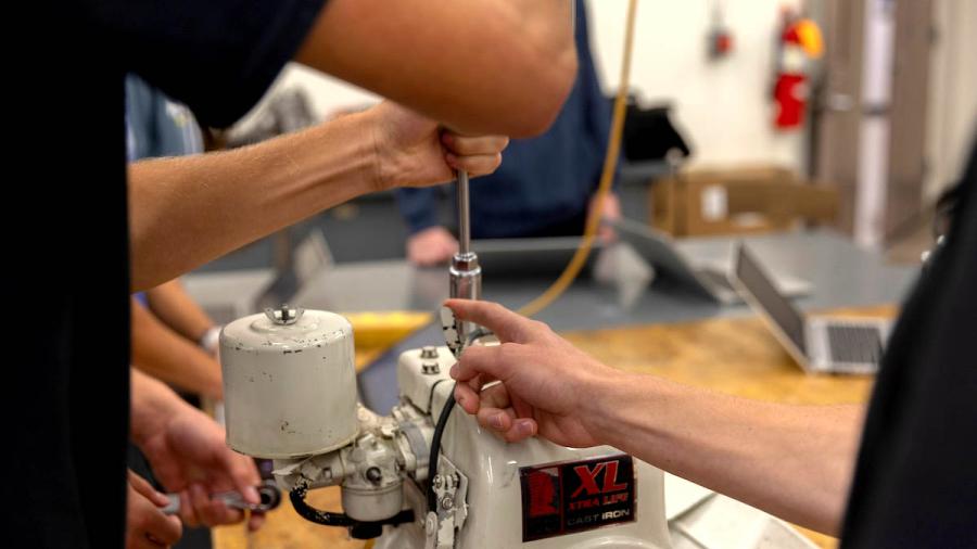 A close-up photo of students hands working on a small engine