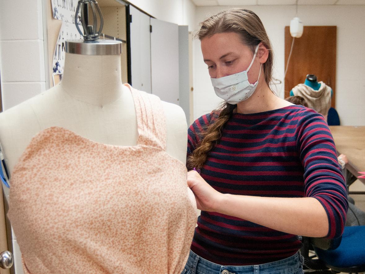 A student adjusts clothing in a fashion and retail lab.